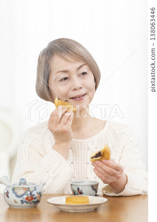 A senior woman drinking tea and snacks in the living room. 138063446
