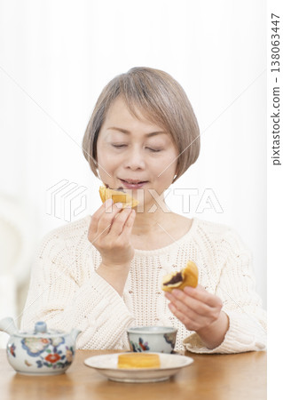 A senior woman drinking tea and snacks in the living room. A senior woman drinking tea and snacks in the living room. 138063447