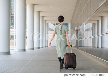 一位女遊客走過城市廣場：她的行李箱和都市旅行景象。 138064006