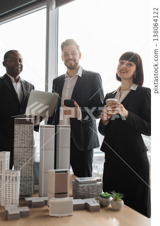 A diverse group of professionals stands in an office, reviewing architectural models and using technology 138064122