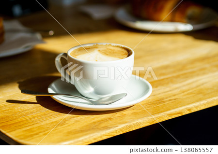 Cappuccino coffee cup on wooden table, minimal cafe scene, warm sunlight, cozy atmosphere, morning drink and relaxation concept 138065557