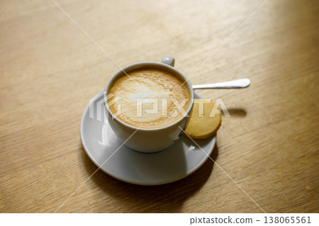 Cappuccino coffee with milk foam and cookie on wooden table, cozy cafe atmosphere, warm light, relaxing morning drink concept Cappuccino coffee with milk foam and cookie on wooden table, cozy cafe atmosphere, warm light, relaxing morning drink concept 138065561