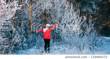 Happy young woman in red jacket enjoying snowy winter forest 138066372