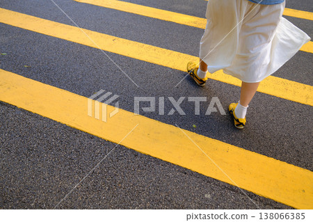 Person walking across road with bold yellow double lines on black asphalt closeup Person walking across road with bold yellow double lines on black asphalt closeup 138066385