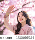 A portrait of a woman in traditional Japanese attire reaching out and looking up at cherry blossoms under a spring sky full of blooming flowers. 138066584