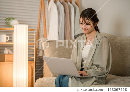 A young Asian woman sitting on a sofa in the living room at night and looking at a laptop A young Asian woman sitting on a sofa in the living room at night and looking at a laptop 138067238