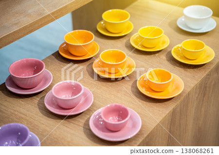 Colorful Stacks of Ceramic Mugs and Plates including yellow, orange, pink and white on Wooden Shelves. 138068261