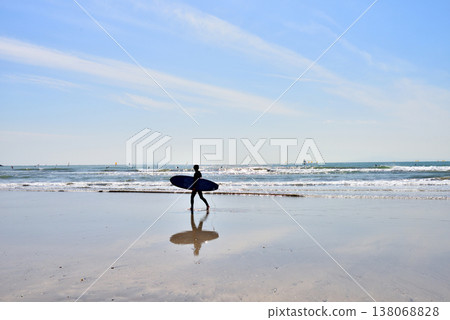 一名衝浪者帶著衝浪板走在沙灘上。 一名衝浪者帶著衝浪板走在沙灘上。 138068828