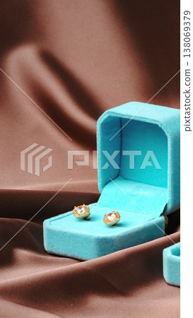 Golden earrings placed in blue jewelry box on brown fabric surface Golden earrings placed in blue jewelry box on brown fabric surface 138069379