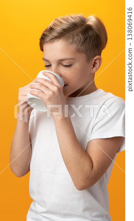Boy drinks from a white cup against a bright yellow background during daytime Boy drinks from a white cup against a bright yellow background during daytime 138069416