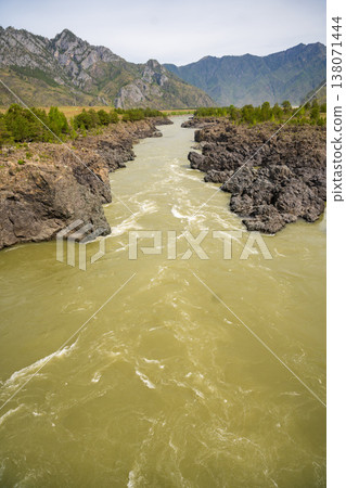 Narrowest and deepest section of Katun river with lava banks in Altai Russia. View from Oroktoy bridge reveals powerful mountain stream cutting through rocky gorge. Narrowest and deepest section of Katun river with lava banks in Altai Russia. View from Oroktoy bridge reveals powerful mountain stream cutting through rocky gorge. 138071444