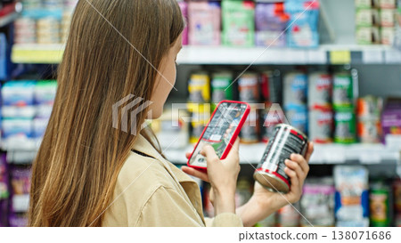Woman Scanning Canned Pet Food With Smartphone And Checking Product Information In Supermarket. Smart Shopping And Retail Technology Concept. 138071686