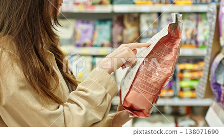 Woman Reading Pet Food Label In Supermarket. Responsible Pet Owner Checking Ingredients Before Purchase. Pet Care And Shopping Concept. Woman Reading Pet Food Label In Supermarket. Responsible Pet Owner Checking Ingredients Before Purchase. Pet Care And Shopping Concept. 138071690