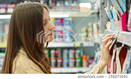 Woman Checking Price Tag On Store Shelf Before Purchase. Budget Shopping And Price Comparison Concept. Woman Checking Price Tag On Store Shelf Before Purchase. Budget Shopping And Price Comparison Concept. 138071691