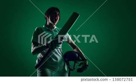 Female cricket player shouting and celebrating holding bat and helmet in green studio light. Female cricket player shouting and celebrating holding bat and helmet in green studio light. 138072781