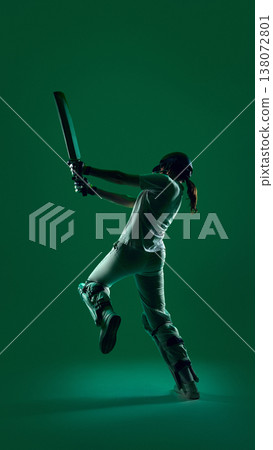 Female cricket batter from back view swinging bat in powerful motion on green background. Female cricket batter from back view swinging bat in powerful motion on green background. 138072801