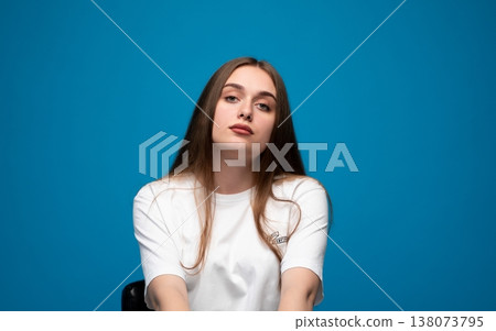 Young serious woman looking at camera on blue background, posing with confidence and calm expression Young serious woman looking at camera on blue background, posing with confidence and calm expression 138073795