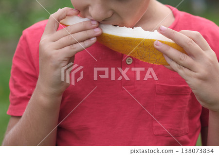 A moment of delight as a boy tastes a ripe melon, his face a picture of satisfaction. This image speaks to the importance of incorporating fruit into daily nutrition. A moment of delight as a boy tastes a ripe melon, his face a picture of satisfaction. This image speaks to the importance of incorporating fruit into daily nutrition. 138073834