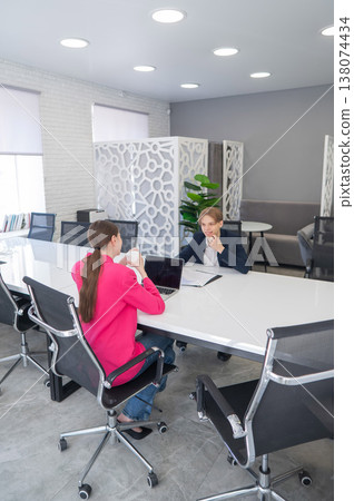 Man and woman talking while sitting at desk in office.  138074434