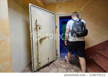 Man With Backpack Entering Underground Bunker Through Heavy Vault Door In Dim Stairwell Man With Backpack Entering Underground Bunker Through Heavy Vault Door In Dim Stairwell 138074522