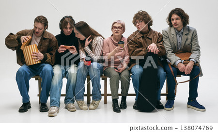 People sitting close together waiting in line with bored expressions in studio. 138074769