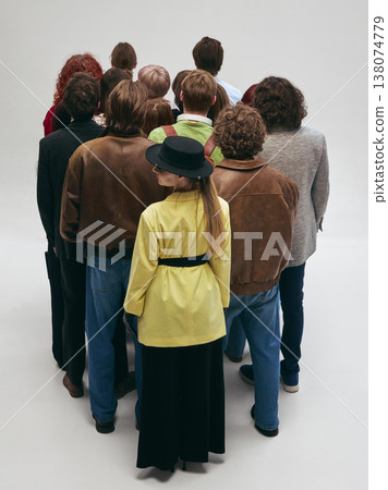 Group of people standing close together from behind with one person looking aside in studio. 138074779