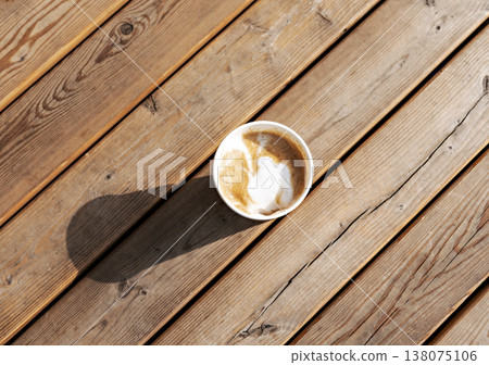 Latte or cappuccino with plant milk in beige paper cup on wooden striped table outside, drinking coffee, light and shadow . Latte or cappuccino with plant milk in beige paper cup on wooden striped table outside, drinking coffee, light and shadow . 138075106