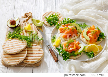 open-faced grilled pita sandwiches with lettuce, smoked salmon slices, avocado, dill, and lemon wedges  138077909