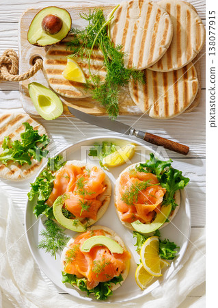 open-faced grilled pita sandwiches with lettuce, smoked salmon slices, avocado, dill, and lemon wedges  138077915
