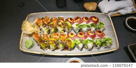 Colorful sushi platter with various rolls and garnishes on dark table Colorful sushi platter with various rolls and garnishes on dark table 138079147