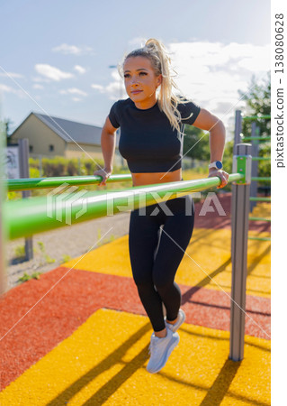 Woman exercising on parallel bars in outdoor fitness area on a sunny day 138080628