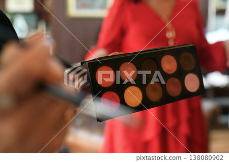 Bridal makeup artist holding eyeshadow palette during cozy morning preparations for wedding 138080902