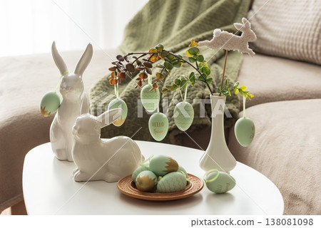 Cozy Easter Living Room Decor with Bunny Figurines and Hanging Eggs on White Table Cozy Easter Living Room Decor with Bunny Figurines and Hanging Eggs on White Table 138081098