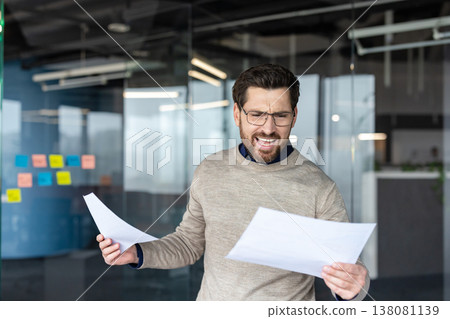 Stressed young businessman feeling frustrated and screaming from anger while holding documents and reading bad news, experiencing financial loss and stress in the modern office Stressed young businessman feeling frustrated and screaming from anger while holding documents and reading bad news, experiencing financial loss and stress in the modern office 138081139
