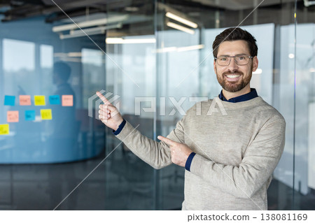 Smiling man pointing with both hands, presenting new ideas and a business strategy with colorful sticky notes on a glass wall in a modern office workplace Smiling man pointing with both hands, presenting new ideas and a business strategy with colorful sticky notes on a glass wall in a modern office workplace 138081169