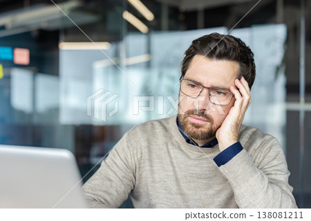 Focused businessman pondering a problem, working on his laptop in a modern office, embodying concentration, stress, and careful consideration for work and tasks Focused businessman pondering a problem, working on his laptop in a modern office, embodying concentration, stress, and careful consideration for work and tasks 138081211