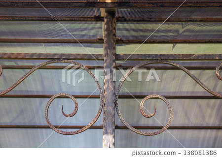 Arched carport roof with transparent plastic panels and black metal frame featuring ornamental iron decorations against blue sky Arched carport roof with transparent plastic panels and black metal frame featuring ornamental iron decorations against blue sky 138081386