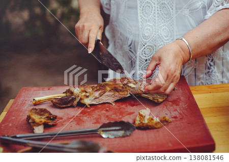 A close-up horizontal shot of a person's hands using a knife to carve a succulent roasted leg of lamb on a red professional cutting board. 138081546