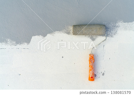 Paint roller with orange handle applying grey paint onto a white textured wall surface. Concept for home renovation, construction, and diy house improvement. Close up view with copy space on left. 138081570