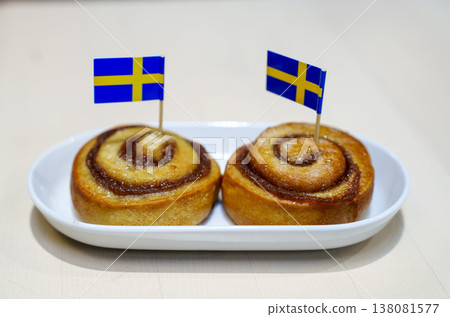 Two traditional Swedish cinnamon rolls, known as kanelbullar, served on a white ceramic plate. Each pastry is decorated with a small Swedish flag. Perfect for fika or Swedish culture concepts. Two traditional Swedish cinnamon rolls, known as kanelbullar, served on a white ceramic plate. Each pastry is decorated with a small Swedish flag. Perfect for fika or Swedish culture concepts. 138081577