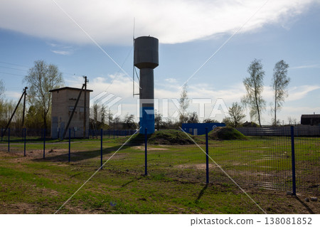 Concrete water tower in the village, the site is fenced with a metal mesh fence 138081852