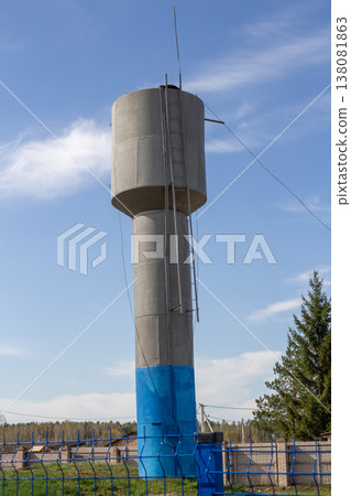 Concrete water tower with blue base and metal ladder against blue sky 138081863