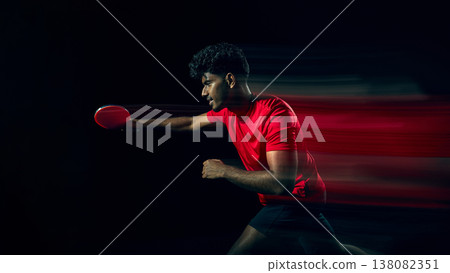 Table tennis player swinging racket with motion blur in dark studio. 138082351