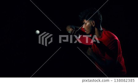 Table tennis player preparing serve with ball in motion in dark studio scene. Table tennis player preparing serve with ball in motion in dark studio scene. 138082385