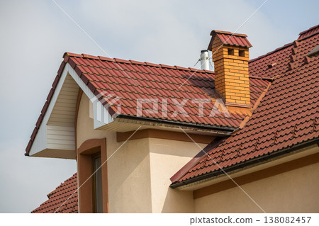 Top of big modern expensive residential house cottage with steep shingled red roof, high brick chimney, stucco walls and attic windows on blue sky copy space background. Investment in future concept. Top of big modern expensive residential house cottage with steep shingled red roof, high brick chimney, stucco walls and attic windows on blue sky copy space background. Investment in future concept. 138082457