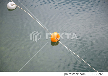Rope with white and yellow restriction markers on water surface for prohibiting of swimming in deep lake or sea. Rope with white and yellow restriction markers on water surface for prohibiting of swimming in deep lake or sea. 138082656