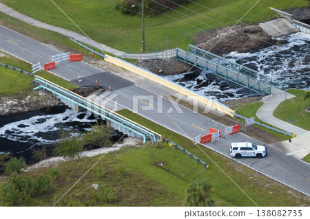 Police car blocking road access at destroyed bridge after hurricane flooding in Florida. Law enforcement patrolling at roadwork site. Reconstruction of damaged road after flood water washed asphalt Police car blocking road access at destroyed bridge after hurricane flooding in Florida. Law enforcement patrolling at roadwork site. Reconstruction of damaged road after flood water washed asphalt 138082735