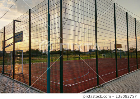 Outdoors mini football and basketball court with ball gate and basket surrounded with high protective fence. 138082757
