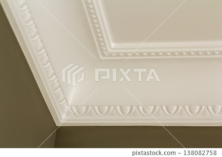 Ornamental white molding decor on ceiling of white room close-up detail. Interior renovation and construction concept. Ornamental white molding decor on ceiling of white room close-up detail. Interior renovation and construction concept. 138082758