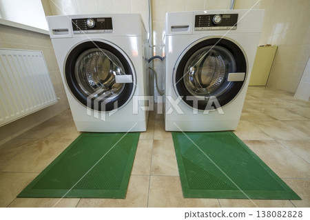 Modern new industrial washing machines in clean tiled bathroom or laundry room on rubber insulation mats. Modern new industrial washing machines in clean tiled bathroom or laundry room on rubber insulation mats. 138082828